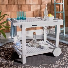 a small white cart with drinks on it in front of a brick wall and rug