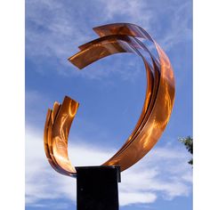 a large metal sculpture on top of a black square stand in front of a blue sky