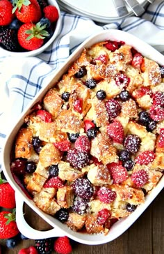 a casserole dish with berries and powdered sugar on top, sitting next to two bowls of strawberries