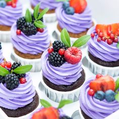 cupcakes with purple frosting and fresh berries on top are arranged in rows