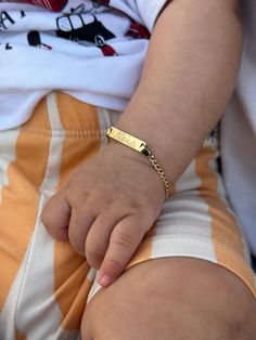 a small child wearing a gold bracelet with a name tag on it's wrist