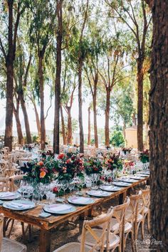 an outdoor dining table set up with place settings and floral centerpieces, surrounded by trees