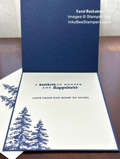 a blue and white greeting card with pine trees on it, sitting on a table