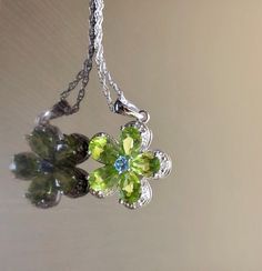 DeKara Designs Silver Metal- Sterling Silver, .925. Stones- 5 Natural Pear Shape Peridot 5 Carats, 1 Round Natural Blue Topaz, 5 Diamonds G-H Color SI2 Clarity 0.02 Carats. Measurements- Necklace is 18 Inches Long. Pendant is Bit Over An Inch Long Including Bail. Beautifully handmade Art Deco inspired halo diamond blue topaz peridot necklace made in sterling silver. There are five natural beautiful green pear shape peridot stones that are all professionally prong set. There is a prong set round Green Flower Pendant Necklace For Anniversary, Green Flower Pendant Fine Jewelry, Green Flower Pendant Jewelry For Anniversary, Green Multi-stone Round Necklace, Green Gemstone Flower Pendant Jewelry, Green Multi-stone Round Necklaces, Fine Jewelry Lime Green Birthstone, Peridot Jewelry With Gemstone Accents For May Birthstone, Fine Jewelry In Green Peridot