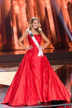 a woman in a red gown standing on stage with her hands on her hips and smiling at the camera