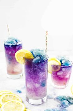 three glasses filled with different colored liquid and lemon slices on top of a white table