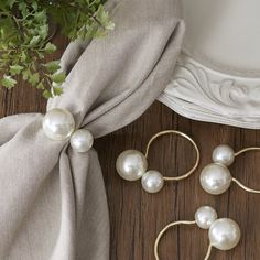 three pairs of pearl earrings on a wooden floor next to a plant and cloth bag