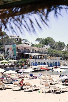 many lounge chairs and umbrellas are set up on the beach in front of a hotel