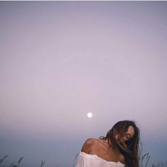 a woman with long hair standing in tall grass at dusk looking off into the distance