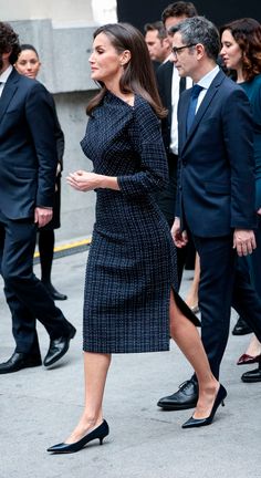 a woman in a black and white dress is walking down the street with other people behind her