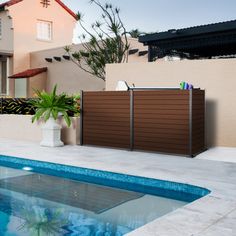 a swimming pool in front of a house with a wooden fence and planter on the side