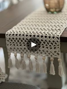 a crocheted table runner with tassels on it and a vase in the background