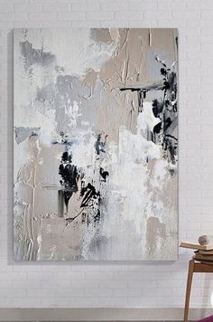 an abstract painting hangs on the wall in a white room with a chair and table