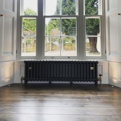 an empty room with a radiator in the middle and large windows above it