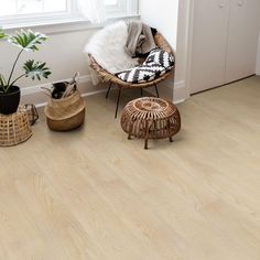 a living room with white walls and wooden flooring next to a chair, potted plant and wicker baskets