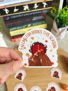 a person holding up a sticker with the words falling for books this season on it