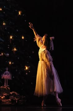 a woman in a white dress standing next to a christmas tree with lights on it