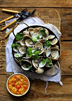 a bowl of clams on a wooden table next to some forks and spoons