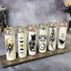 five jars with different designs on them sitting on a wooden tray next to flowers and candles