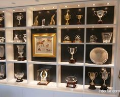 a display case filled with lots of trophy cups and vases on top of white shelves