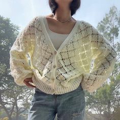 a woman standing in front of some trees wearing a white sweater and ripped denim shorts