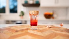 a glass filled with red liquid sitting on top of a wooden table in a kitchen