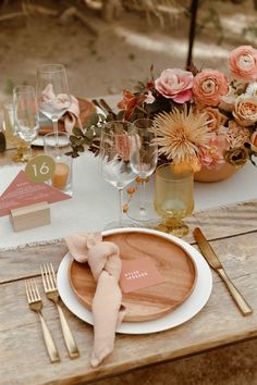 a wooden table topped with a white plate covered in flowers next to a vase filled with pink and orange flowers