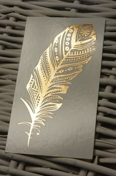 a card with a gold feather on it sitting on a wicker tablecloths