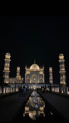 people are standing in front of a building at night with lights on the buildings and water reflecting off the ground