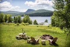 there are four wooden chairs around a fire pit in the grass near some trees and mountains