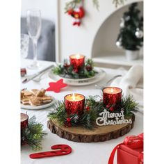 a christmas table setting with red candles and greenery