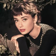 a woman with short hair posing in front of a tree