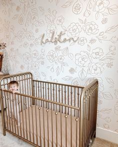 a baby in a crib next to a wall with flowers on it