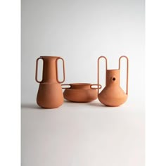 three vases and one bowl on a white surface with the handles extended up to allow them to hold food