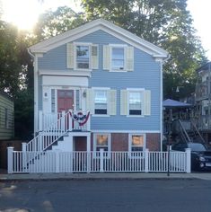 a blue two story house with white picket fence and car parked on the street in front of it