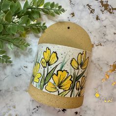 a yellow and white flowered pot sitting on top of a marble counter next to a plant