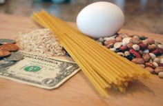 pasta, nuts, and an egg are on a table next to one dollar bill