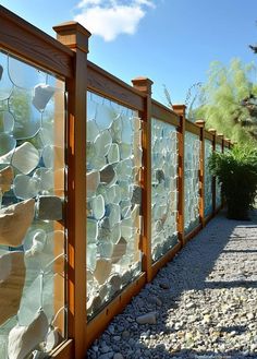 a fence made out of glass and wood with rocks on the ground next to it