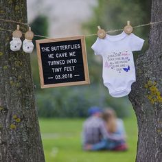 two baby onesuits hanging from clothesline next to tree with sign saying the butterflies he gave me turned into tiny feet