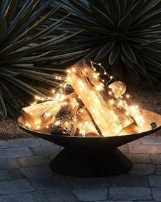 a black bowl filled with lights on top of a stone floor next to plants and trees