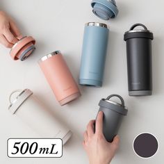 a person holding a cup next to several different colored tumbles on a white table