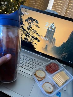 a person is holding a cup with some food in front of their laptop computer on the desk