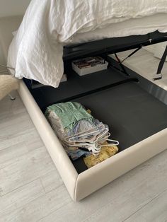 a bed with an open drawer underneath it on the floor next to a white pillow