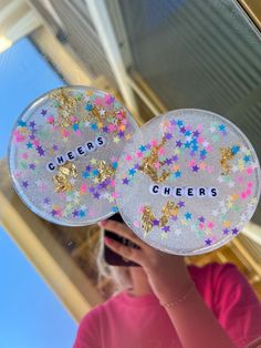 a girl is holding up two plates with glitter stars on them that say cheers and cheers