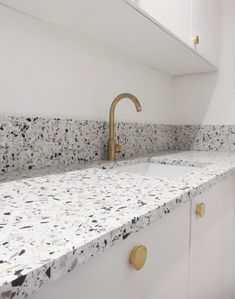 a white counter top with gold faucet in the middle and black speckles on it