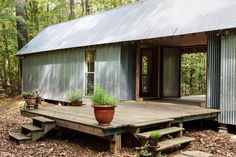 a wooden deck with potted plants on it in front of a metal building surrounded by trees