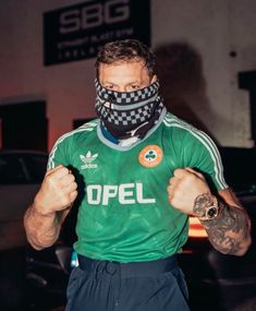 a man wearing a green shirt and black pants with a checkered face mask on