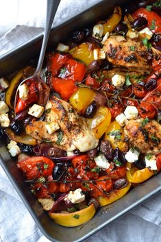 a pan filled with chicken and vegetables on top of a white table cloth next to a fork