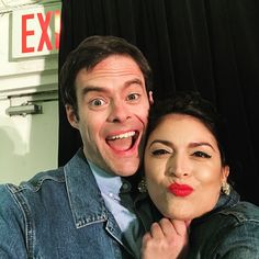 a man and woman are posing for a photo in front of a black curtain with the exit sign behind them