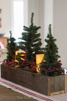 a wooden box filled with christmas trees on top of a table next to a candle